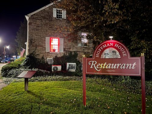 A stone building at night with a lit window and a sign reading "Hoffman House Restaurant - Circa 1711."