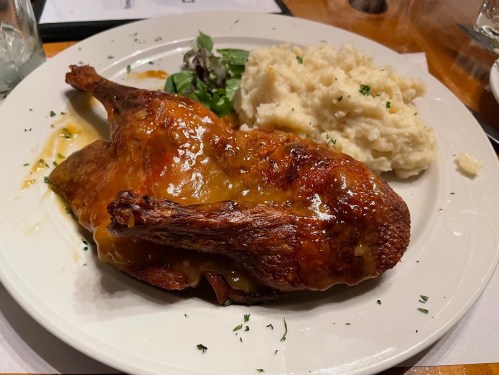 A plate featuring roasted duck with a glossy sauce, served with mashed potatoes and a side of greens.