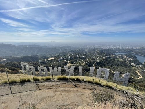 View of the Hollywood sign with a scenic landscape and city skyline in the background under a clear blue sky.