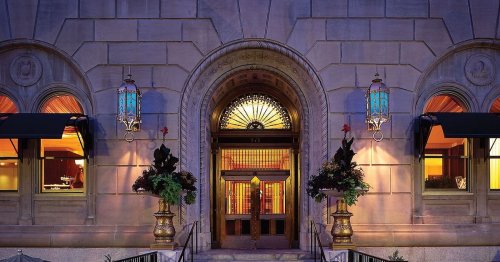 Elegant entrance of a historic building, featuring ornate doors, decorative lanterns, and lush floral arrangements.