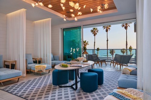 A stylish lounge area with blue furniture, a round table, and large windows overlooking palm trees and the ocean.