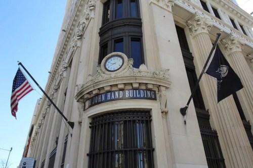 Exterior of the John Hand Building featuring a clock and American flag, showcasing architectural details.