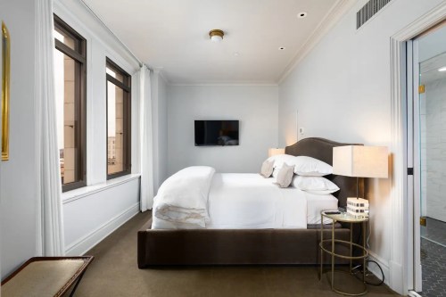 Cozy bedroom with a bed, bedside table, TV on the wall, and large windows letting in natural light.