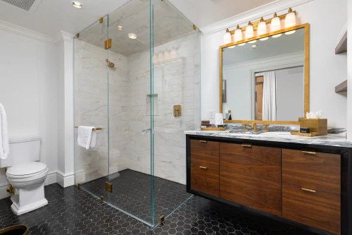 Modern bathroom featuring a glass shower, marble accents, wooden vanity, and stylish lighting.