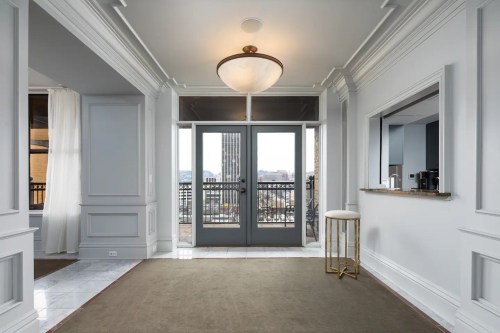 Bright entryway with large doors, elegant decor, and a view of the city skyline through the windows.