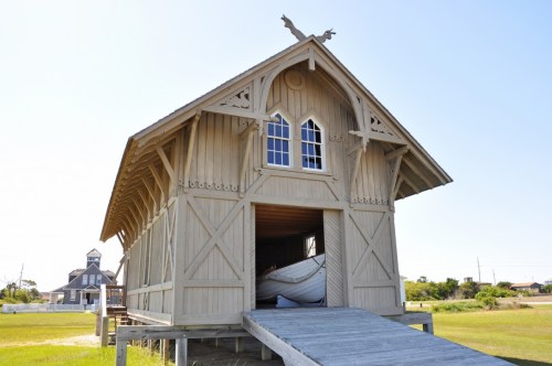 A wooden boathouse with a ramp, featuring intricate architectural details and a boat inside, set against a clear sky.