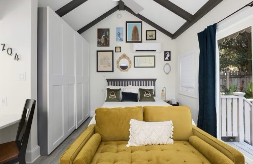 Cozy bedroom with a bed, framed art on the walls, a yellow couch, and a door leading to an outdoor area.