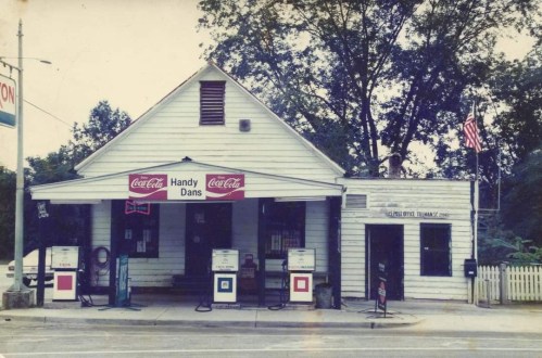 A vintage convenience store named "Handy Dans" with Coca-Cola signage, surrounded by trees and an American flag.