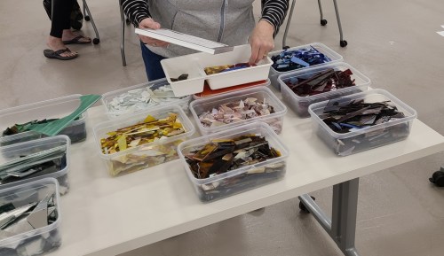 A person sorting colorful glass pieces in containers on a table during a crafting session.