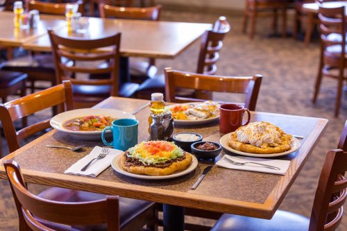 A table set with three plates of colorful food, two mugs, and condiments in a cozy restaurant setting.