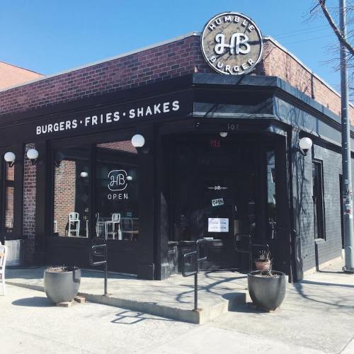 Exterior of Humble Burger restaurant, featuring a sign, open door, and outdoor seating area.