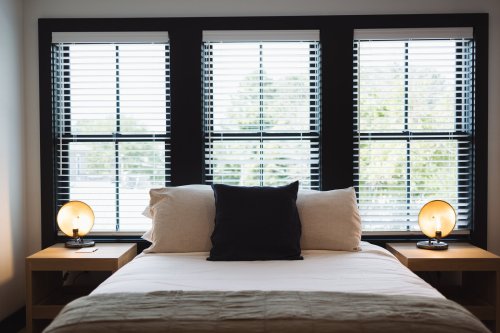 Cozy bedroom with a bed, two bedside lamps, and large windows with blinds letting in natural light.