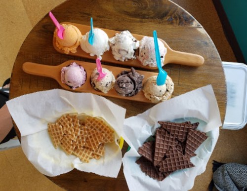 A wooden board with six ice cream scoops and two plates of waffle cones on a table.