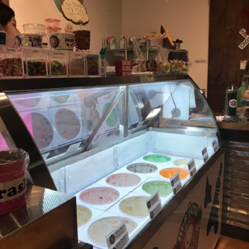 A display of various ice cream flavors in a shop, with colorful tubs and toppings visible in the background.