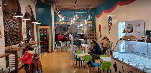 A cozy ice cream shop with colorful decor, tables, and customers enjoying treats in a lively atmosphere.