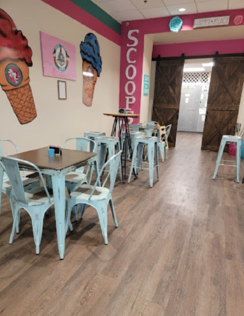 Bright ice cream shop interior with pastel blue tables and chairs, colorful wall art, and a rustic wooden door.