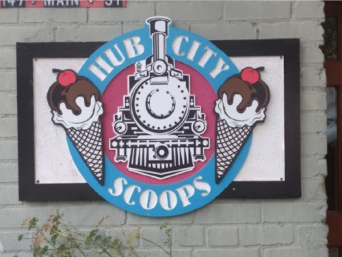 Sign for "Hub City Scoops" featuring a train and ice cream cones with chocolate scoops and cherries on top.