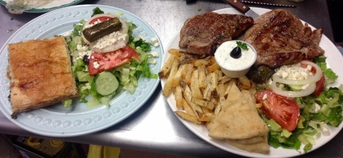 A plate of grilled meat with salad, fries, and pita, alongside a slice of baklava on a blue plate.