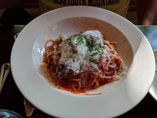 A plate of spaghetti topped with marinara sauce, grated cheese, and fresh herbs, served on a white dish.