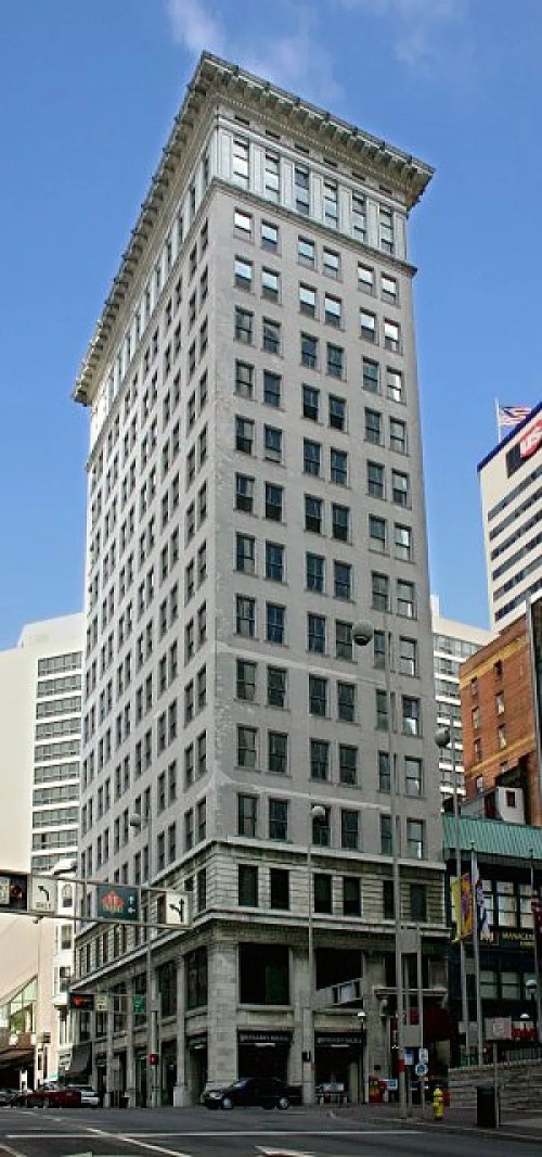 Historic tall building with a decorative cornice, set against a blue sky and modern cityscape.