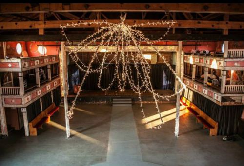 A spacious, vintage theater with a central stage, adorned with string lights and balcony seating on either side.