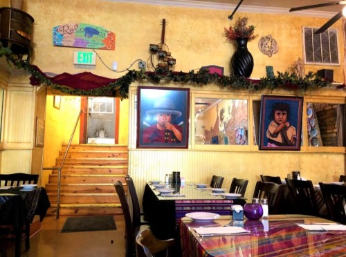 Interior of a restaurant featuring colorful artwork, wooden tables, and a staircase leading to an upper level.