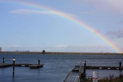 A serene waterfront scene featuring a rainbow arching over calm waters and wooden docks.