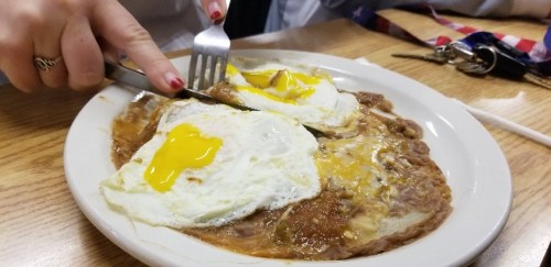 A plate of refried beans topped with two sunny-side-up eggs, with a hand cutting into the eggs.