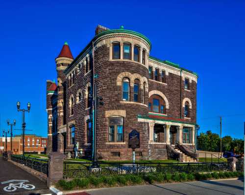 Historic stone building with a turret, green roof, and decorative windows, set against a clear blue sky.