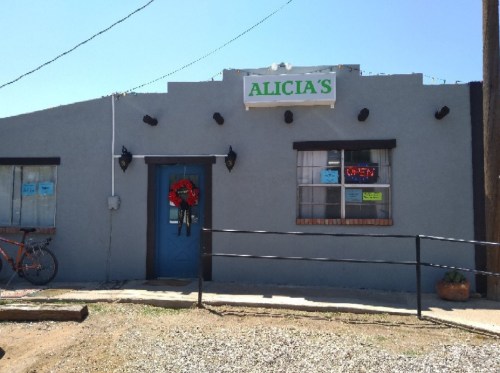 Alicia's storefront with a blue door, wreath, and "OPEN" sign, set against a clear blue sky.