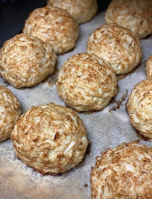 Freshly baked coconut macaroons on a parchment-lined baking sheet, golden brown and round in shape.