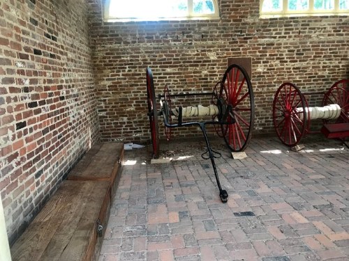 Interior of a brick room featuring wooden benches and vintage equipment with large red wheels.