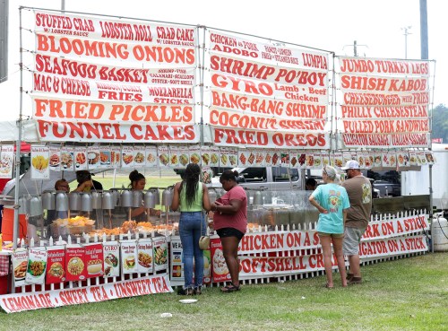 A food stall with various menu items displayed on bright red signs, featuring fried foods and sandwiches.