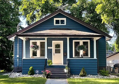 A charming blue house with a front porch, flower pots, and a well-maintained yard under a sunny sky.
