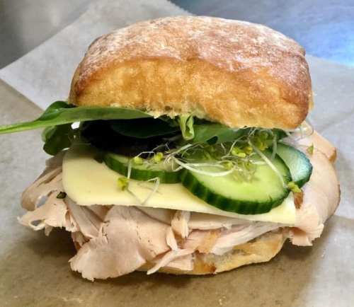 A sandwich with sliced turkey, cucumber, cheese, and greens on a toasted bun, served on parchment paper.