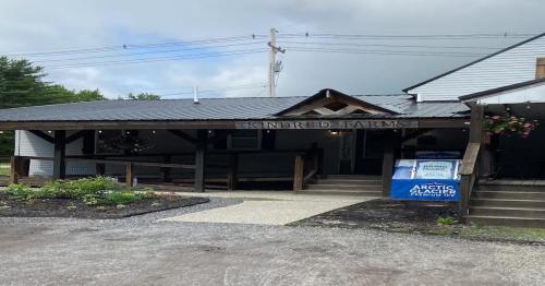 A rustic farm store with a covered porch, sign reading "Kindred Farms," and a cooler for ice outside.