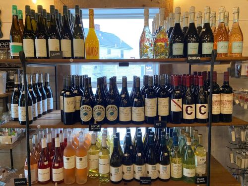 A display of various wine bottles on shelves, featuring red, white, and sparkling options, with a window in the background.