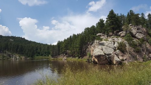 A serene lake surrounded by rocky cliffs and lush green trees under a partly cloudy sky.