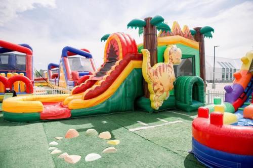 Colorful inflatable dinosaur-themed playground with a slide and various play structures on green turf.