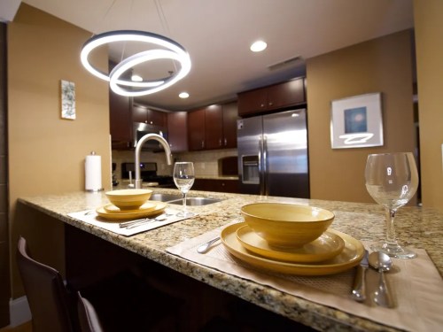 Modern kitchen with granite countertops, yellow dishware, and a stylish pendant light above a dining area.