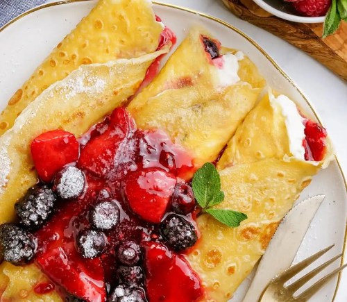 Delicious crepes filled with cream and topped with mixed berries and a berry sauce, garnished with mint.