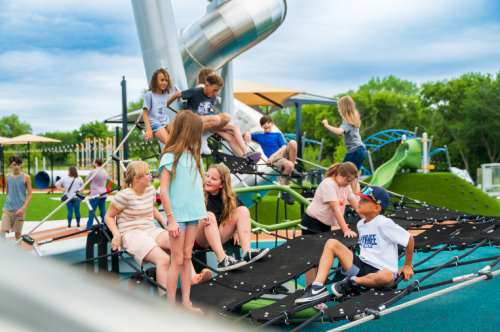 A group of children playing on a colorful playground structure with slides and climbing features on a sunny day.