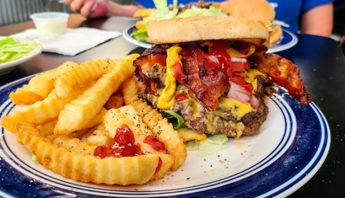 A juicy burger with bacon, lettuce, and condiments, served with crinkle-cut fries on a blue plate.