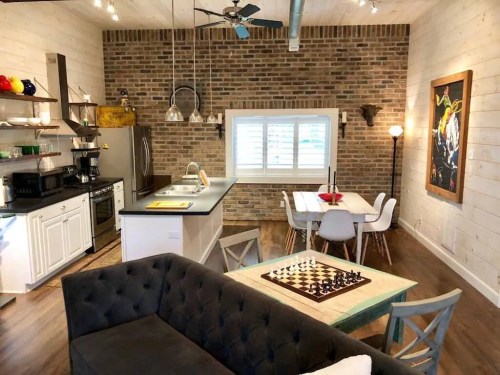 Cozy kitchen and living area with brick walls, modern appliances, a chessboard, and a dining table.