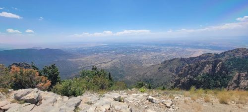 A panoramic view of a valley and distant mountains under a clear blue sky, with rocky terrain in the foreground.