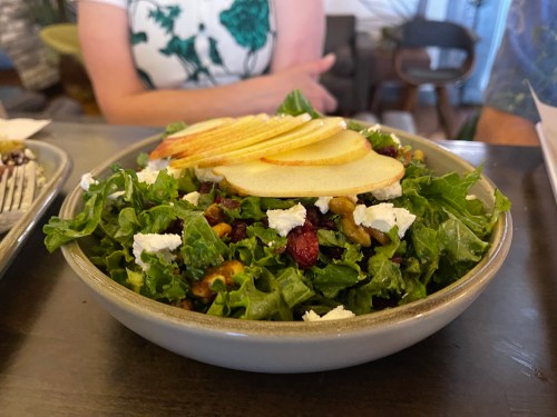 A fresh salad with greens, sliced apples, walnuts, cranberries, and goat cheese in a bowl on a table.