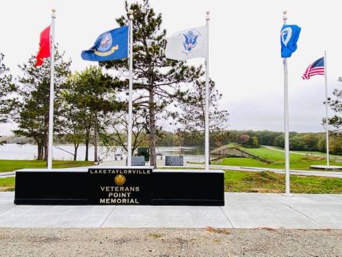 A memorial with flags representing different branches of the military, overlooking a lake at Lake Taylorville.