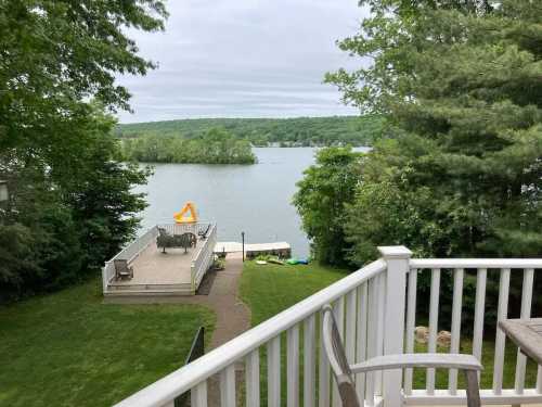 View of a serene lake surrounded by greenery, with a deck and seating area in the foreground.