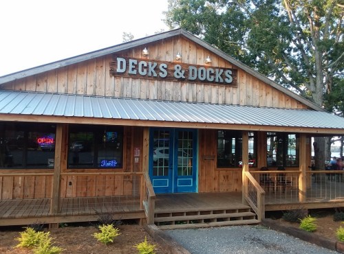 A wooden restaurant exterior with a sign reading "Decks & Docks," featuring blue doors and a welcoming atmosphere.
