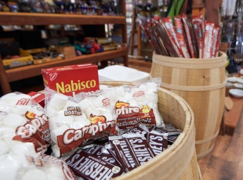 A wooden barrel filled with bags of marshmallows and chocolate bars, with a box of Nabisco cookies in the background.